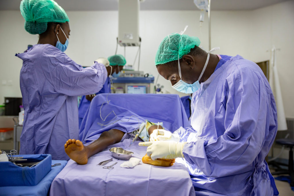 A surgeon works on the lower leg of a child with an anaesthetist monitoring.